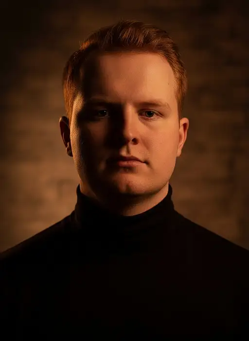Close-up portrait of a young male model in a black turtleneck, cinematic side lighting creating warm shadows and sharp focus.